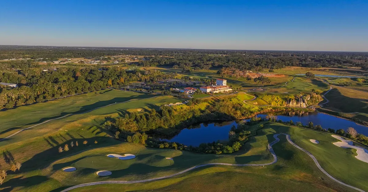 Aerial view of a luxury golf course community featuring manicured fairways, sand bunkers, serene water features, and an elegant clubhouse surrounded by lush ...